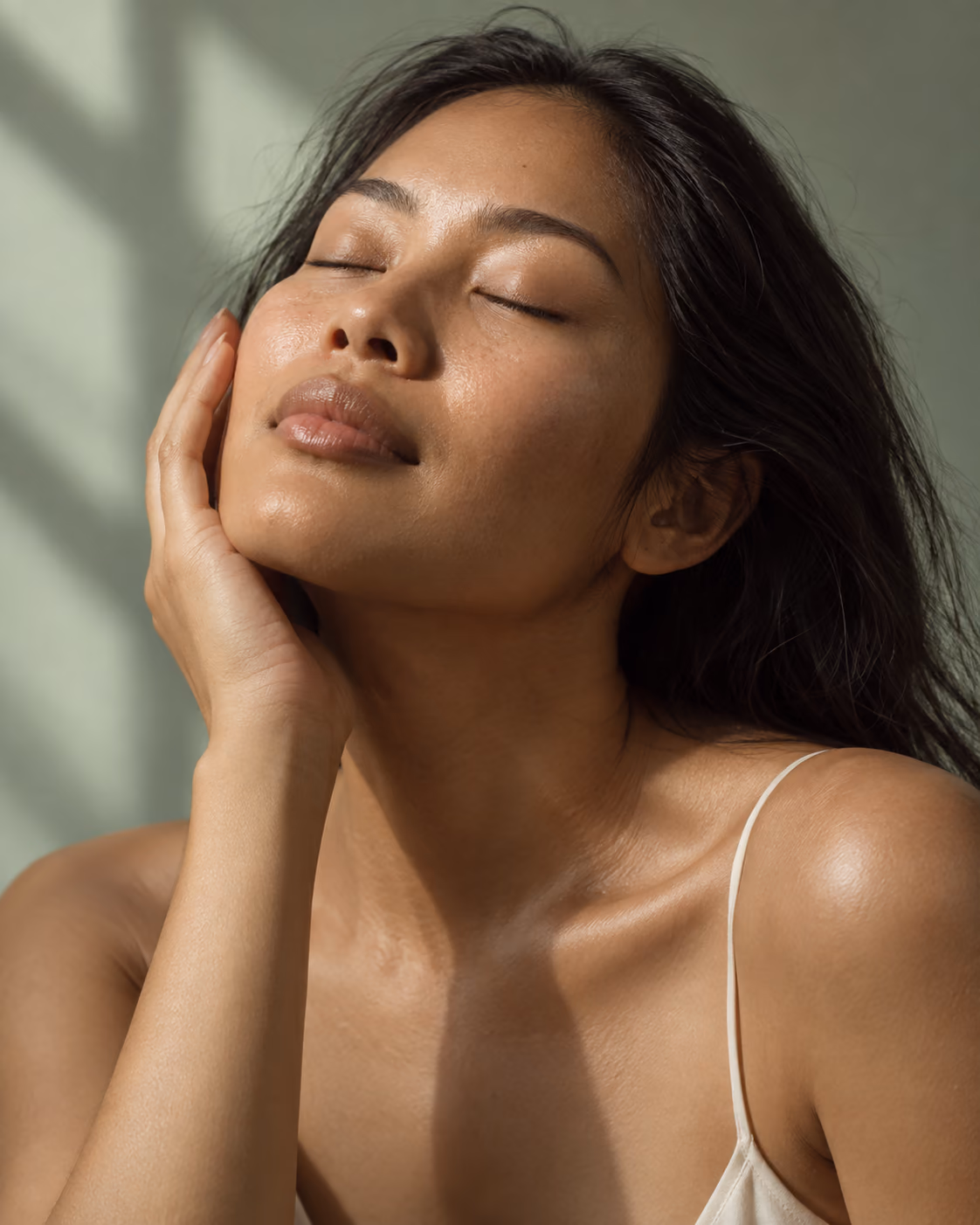 A woman resting her hand against her cheek, eyes closed in the sunlight